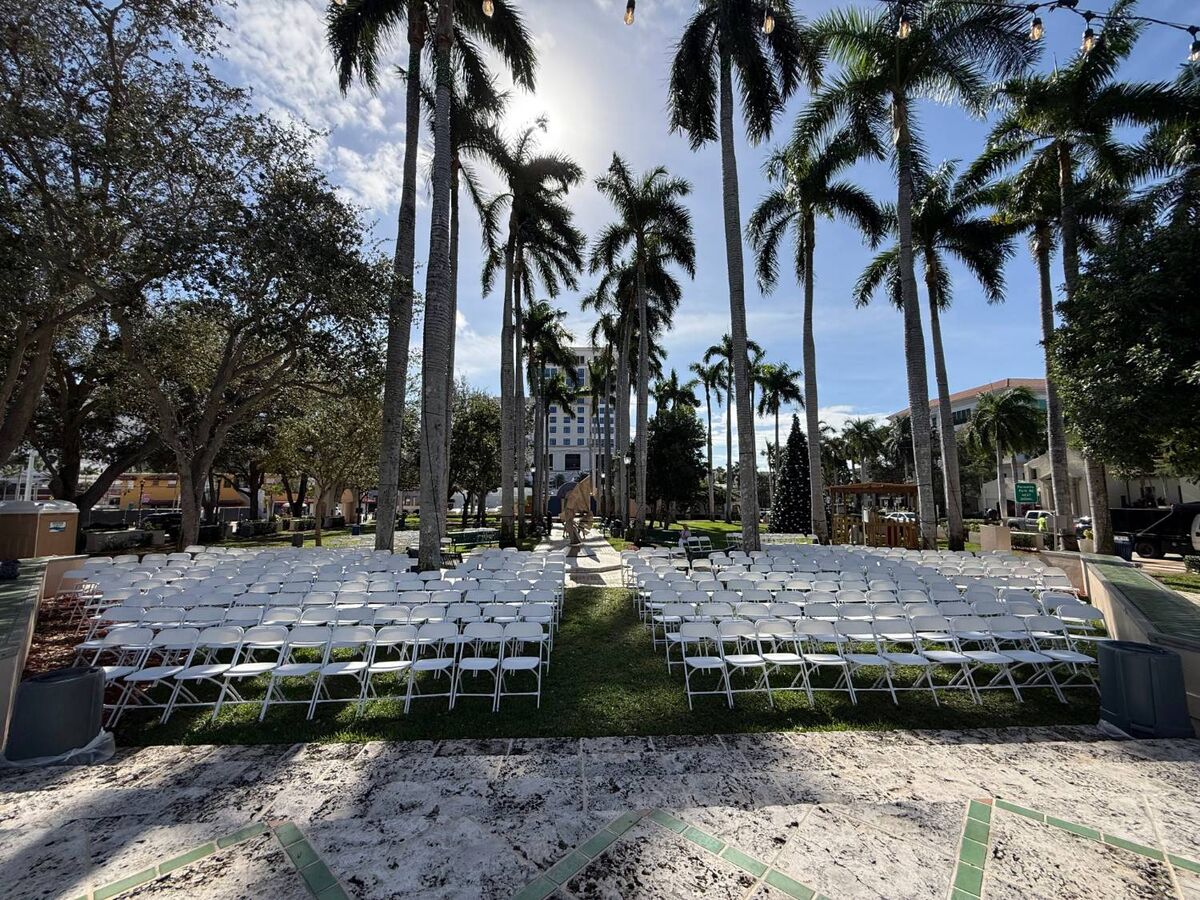 Rows of white folding chairs set up on a lawn under palm trees for an outdoor ceremony