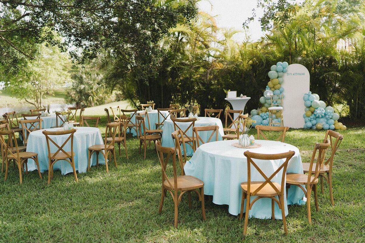 Cross-back wood chairs around round tables with light blue linens on a lawn for a bar mitzvah