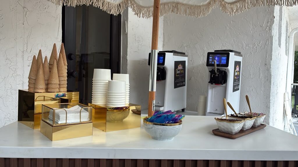 Bash soft serve cart with a fringed umbrella, two machines, cones and cups on gold stands, and a toppings tray