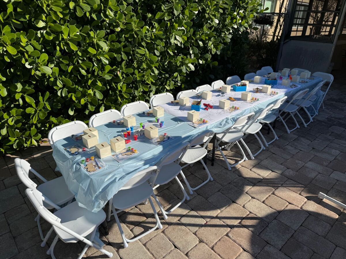 Long tables with kids-size white folding chairs and craft activities set out for a birthday party
