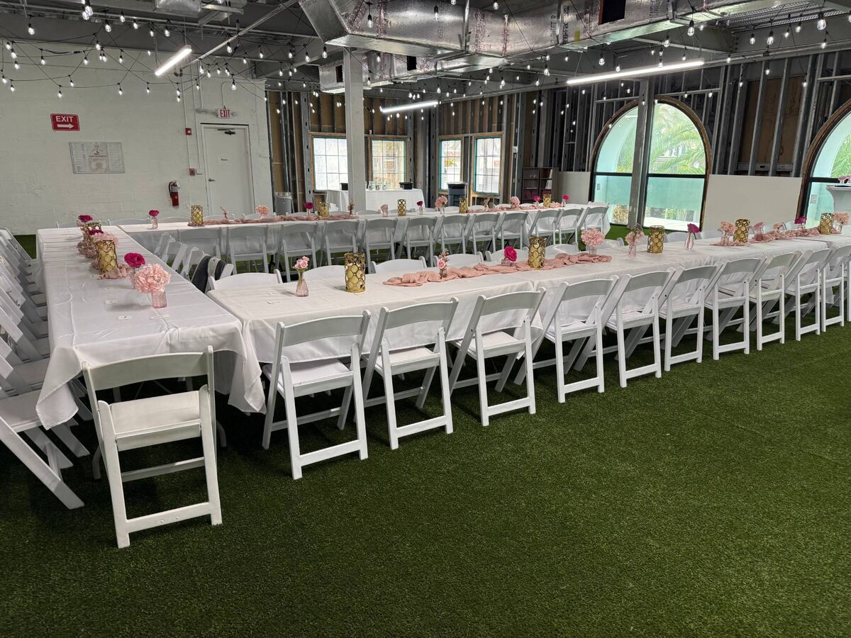 Long tables with white linens, pink runners and gold centerpieces, lined with white folding chairs
